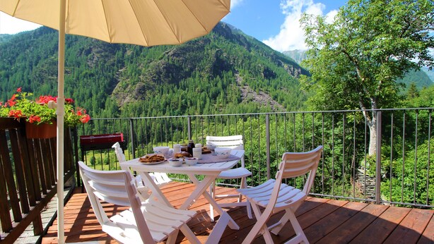A wooden deck with white chairs and a table, overlooking a mountainous landscape. - Baus's Cabins. A mountain cabin in the village—warm, cozy, and offering breathtaking views. (Turin)