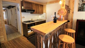 A kitchen with wooden cabinets, a gas stove, a sink, and a bar area with stools. - Baus's Cabins. A mountain cabin in the village—warm, cozy, and offering breathtaking views. (Turin)