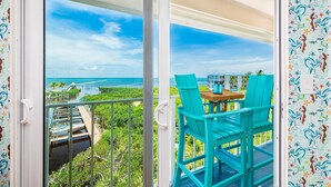 Un balcon avec des chaises turquoise et une table, d’où l’on peut admirer une vue sur la côte, avec un bâtiment en arrière-plan.