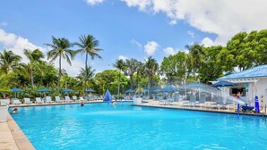 Une piscine entourée de palmiers, avec des chaises longues et des parasols.