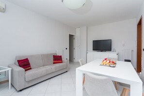 Un salon moderne avec un canapé, une table à manger dressée, un téléviseur et un plafond blanc.