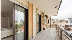 Ein Balkon mit Glastür, einem weißen Sofa und Blick auf die Stadtlandschaft.