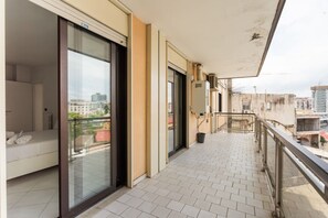 Ein Balkon mit Glastür, einem weißen Sofa und Blick auf die Stadtlandschaft.