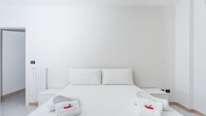 Ein schlicht eingerichtetes Hotelzimmer mit einem großen Bett, weißer Bettwäsche, einem Nachttisch und einer Heizung.
