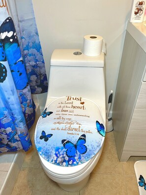 Eine Toilette mit einem dekorativen Deckel, der einen Vers aus Sprichwörter 3,56 und blaue Schmetterlinge zeigt.