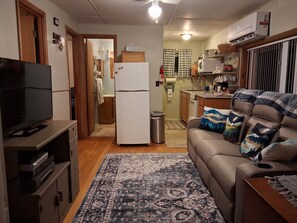 A compact living space with a television, sofa, and kitchen area. - The Lady Slipper Lodge - Old Timey cabin retreat with Starlink & Dish (Franklin)