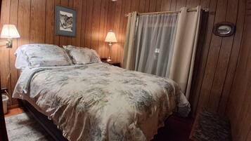 A bedroom with wooden paneling, a bed with floral bedding, two bedside lamps, a nightstand, and a framed picture on the wall.