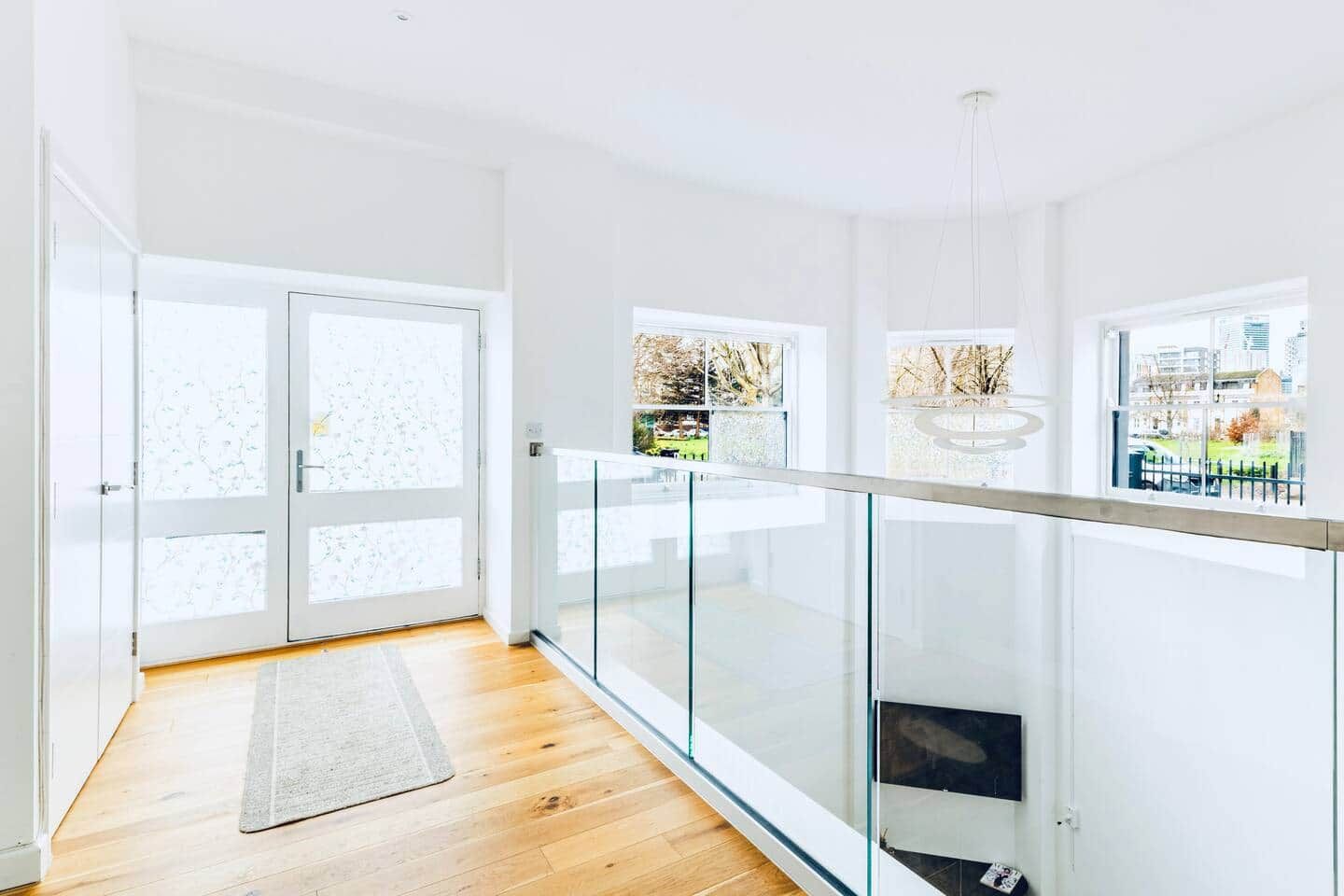 A modern interior with a wooden floor, glass railing, and a view through large windows.