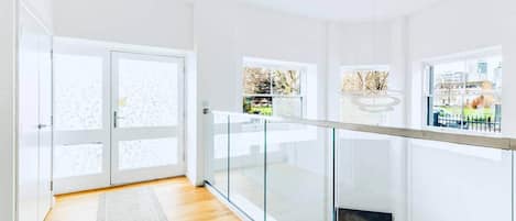 A modern interior with a wooden floor, glass railing, and a view through large windows.