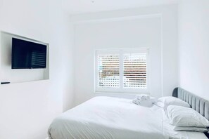 Ein Schlafzimmer mit einem Bett, einem Fernseher und einem Fenster mit Jalousien.
