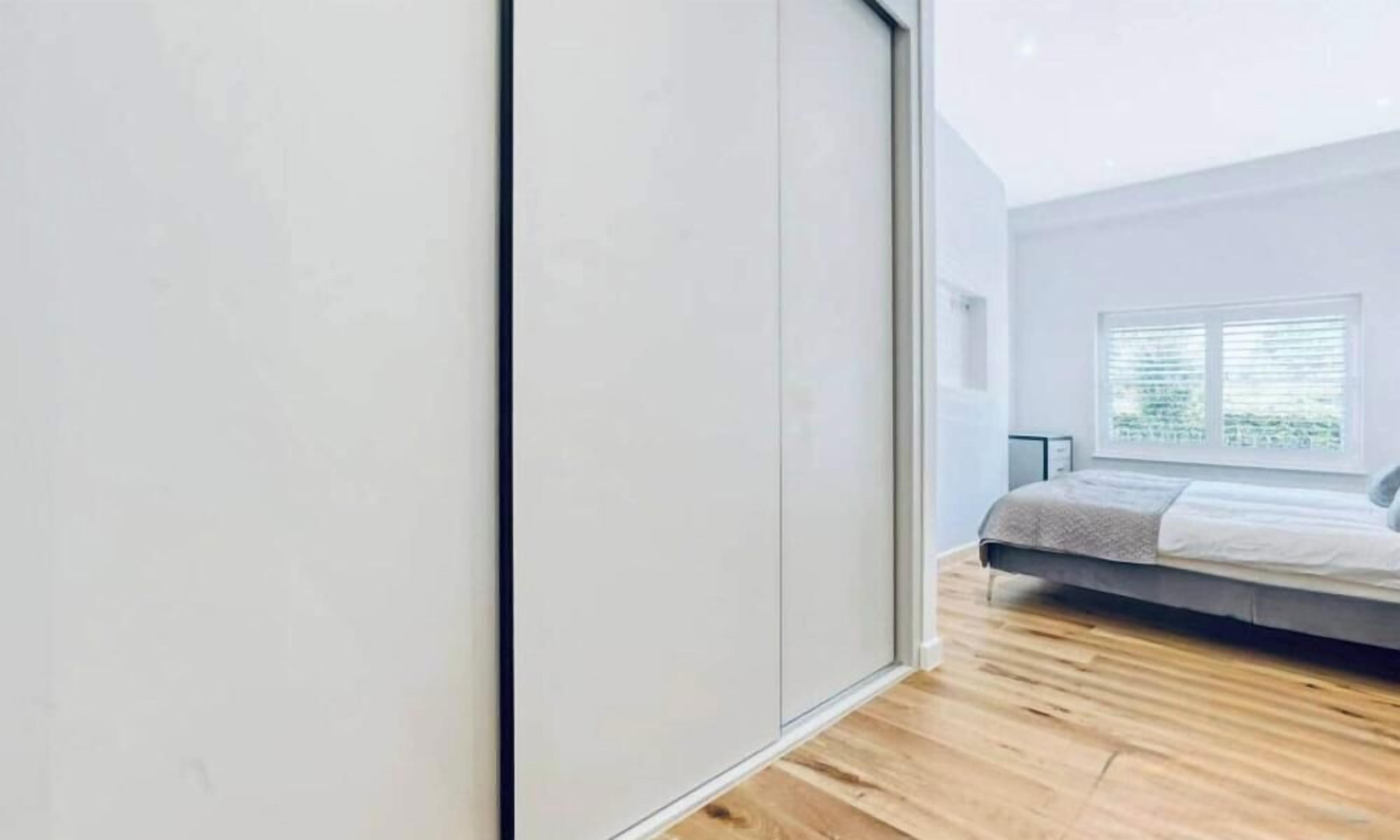 A bedroom with a bed, a window with blinds, and a wooden floor.