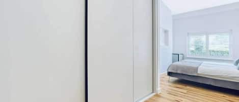 A bedroom with a bed, a window with blinds, and a wooden floor.