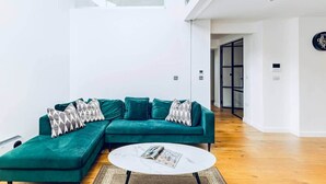 Ein modernes Wohnzimmer mit einem smaragdgrünen Ecksofa, einem runden Couchtisch und einem großen Fenster.