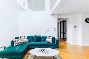 Ein modernes Wohnzimmer mit einem smaragdgrünen Ecksofa, einem runden Couchtisch und einem großen Fenster.