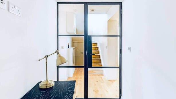Ein Zimmer mit Schreibtisch, Lampe und einer Schiebetür zu einer Treppe.