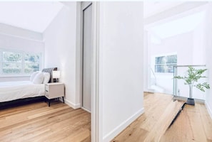 A modern bedroom with a bed, bedside table, lamp, and a potted plant. - Detached Family Home with Free Parking (London)