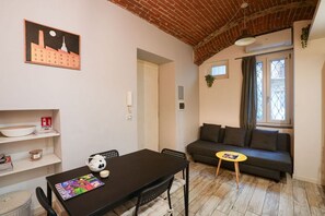 A room with a dining table, a sofa, and a window with curtains. - Torino Centro | Saluzzo 17 Apartment (Torino)