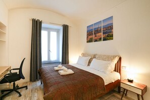Ein Hotelzimmer mit einem Bett, einem Schreibtisch, einem Sessel, einem Fenster mit Vorhängen und zwei Bildern an der Wand.