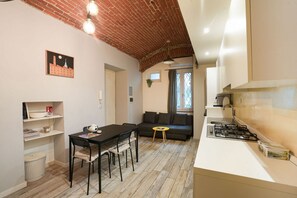 A compact living space with a dining area, a sofa, a small table, and a kitchen area with a stove. - Torino Centro | Saluzzo 17 Apartment (Torino)