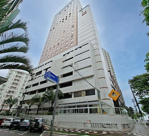 Um edifício alto com vários andares, uma placa de rua azul e um sinal amarelo com um símbolo de chapéu.