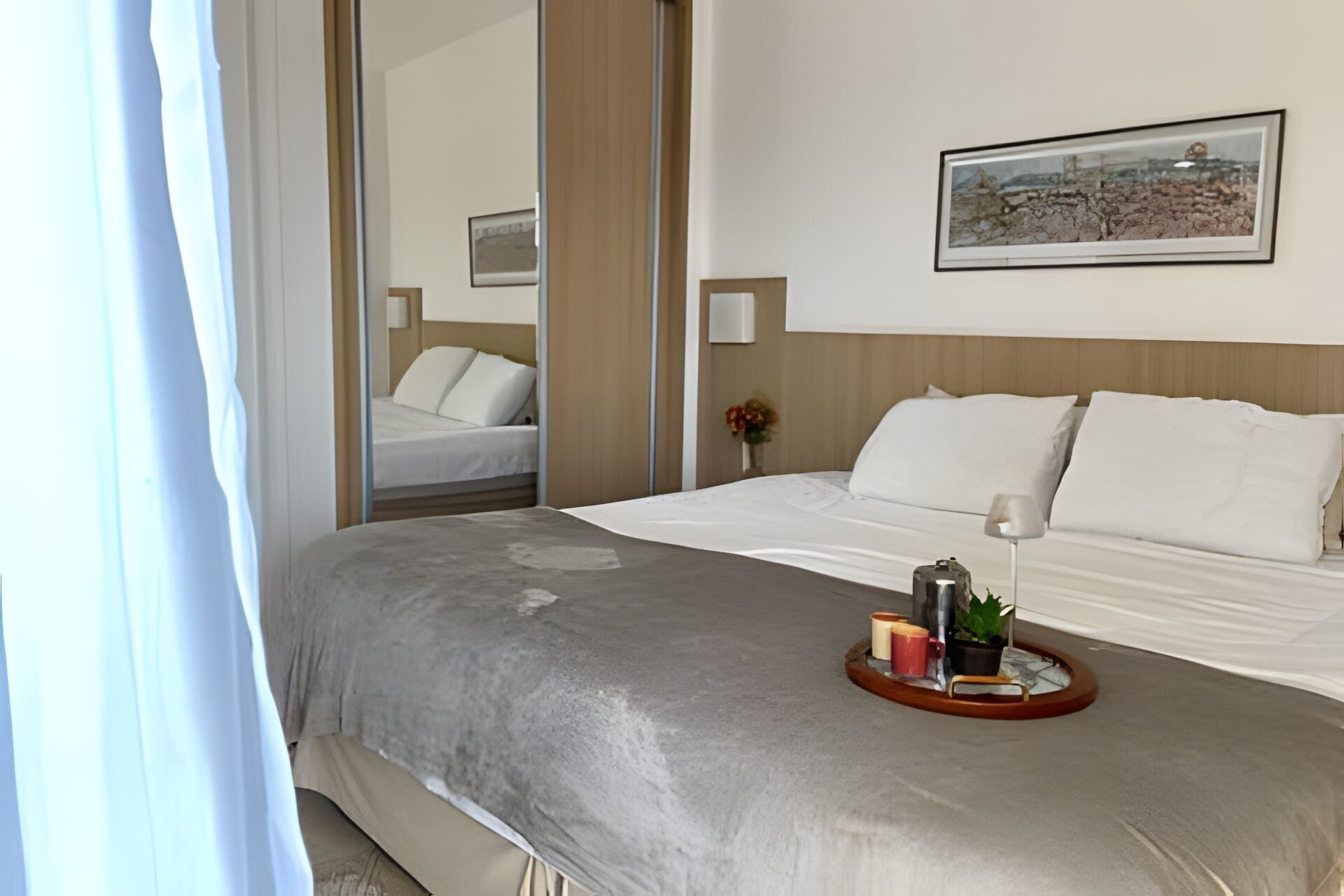 A hotel room with a bed, a bedside table with a tray, a lamp, and a framed picture on the wall.