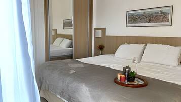 A hotel room with a bed, a bedside table with a tray, a lamp, and a framed picture on the wall.