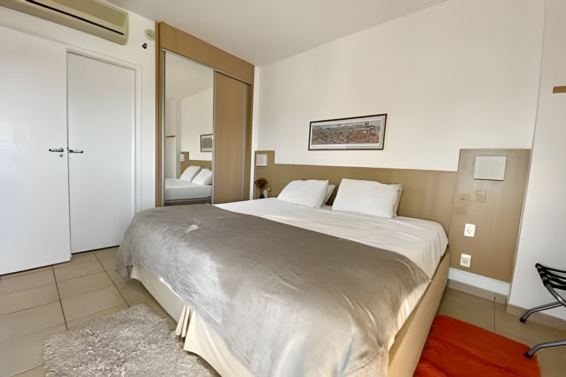 Habitación de hotel con una cama grande, un armario, un espejo y un cuadro en la pared.