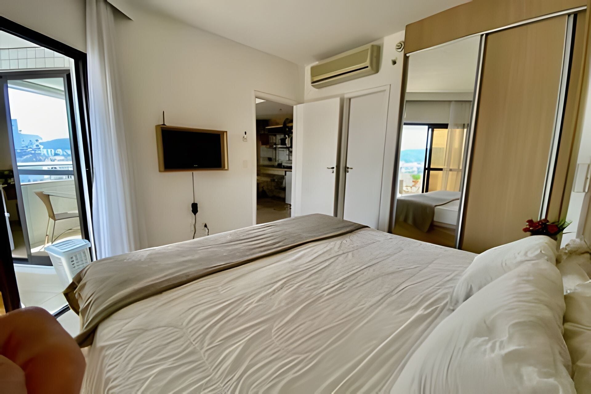 Habitación de hotel con cama, televisión montada en la pared, armario y balcón con vistas.