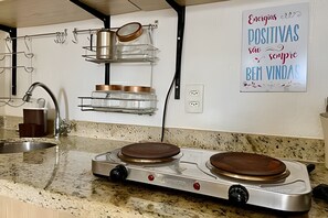 Una cocina con estufa a gas, un lavamanos y un estante empotrado con utensilios de cocina.