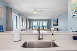 Eine moderne Küche mit einer Edelstahl-Spüle, einem Deckenventilator und Meerblick durch große Fenster.