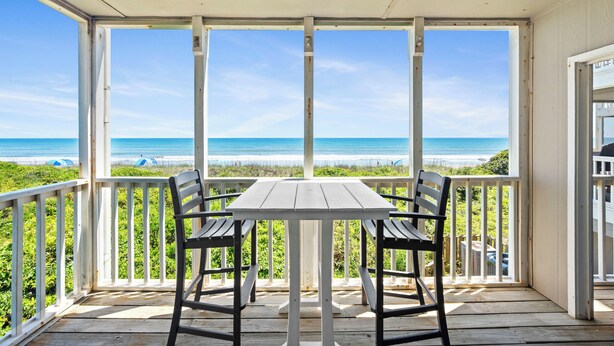 Un espacio al aire libre cubierto con una mesa y sillas, con vista a la playa.