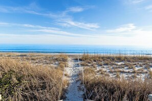 Ein Strandweg, der zum Meer führt, mit Sand und trockenem Gras.
