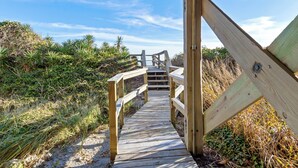 Un paseo marítimo de madera que lleva a una zona de playa con vegetación natural.