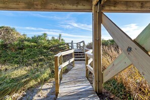 Ein hölzerner Steg führt zu einer Strandbucht mit natürlicher Vegetation.