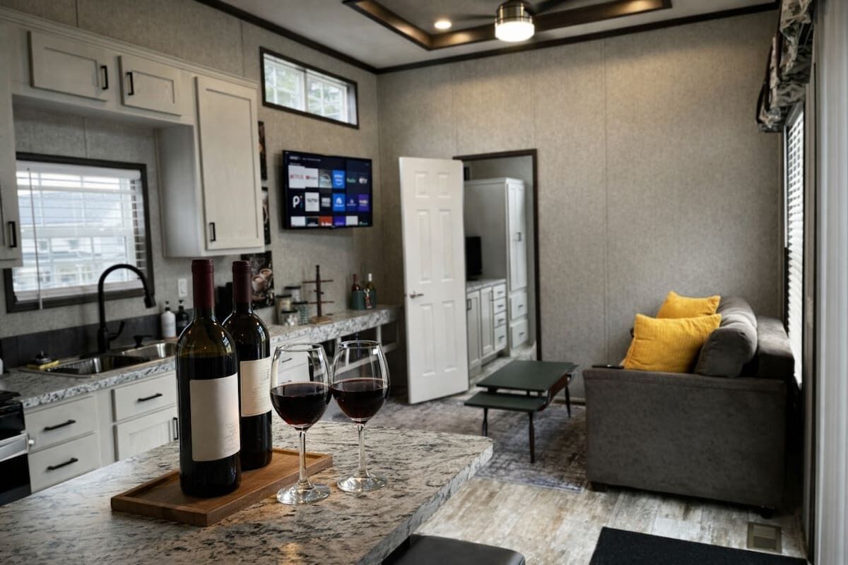 A modern kitchen with a marble countertop, wine bottles, glasses, and a flat-screen TV.