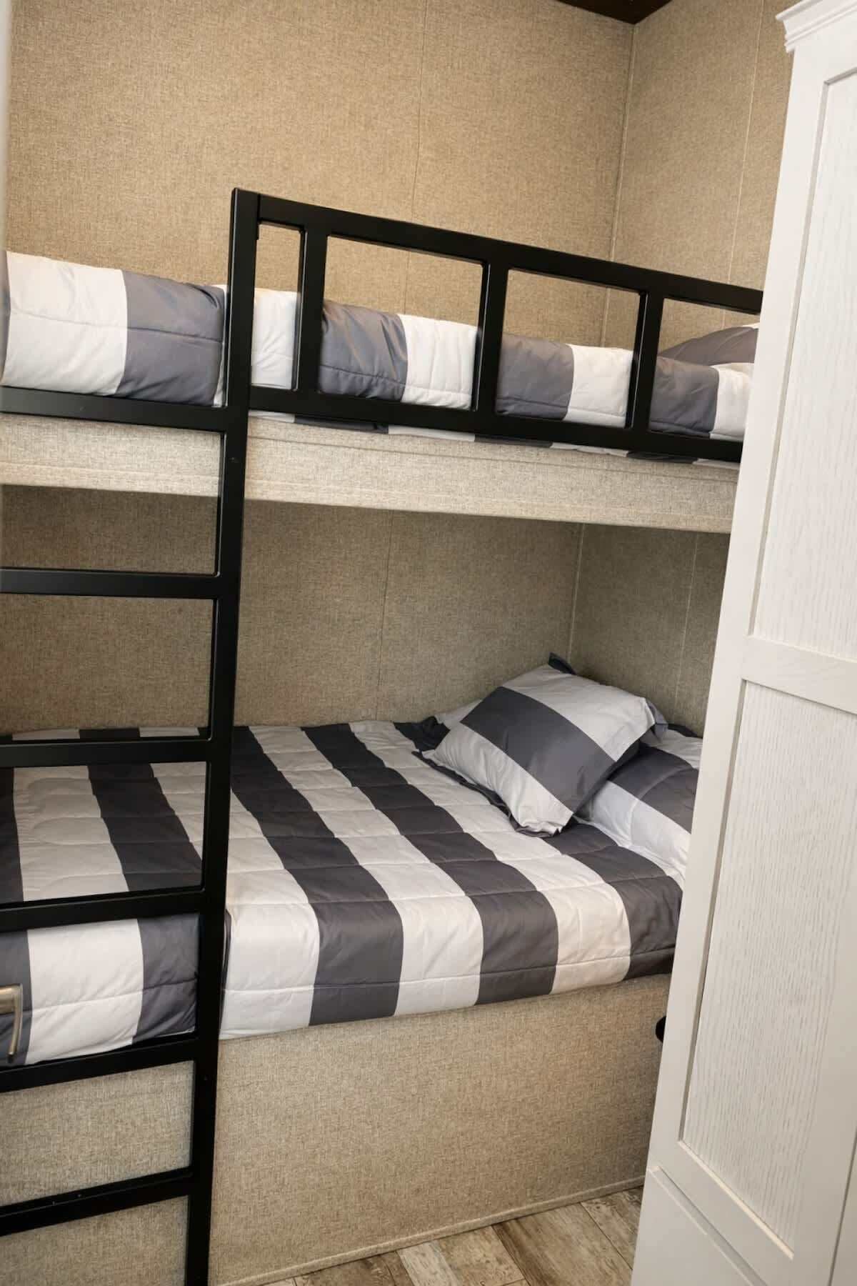 Dans la chambre, on trouve un lit superposé avec un motif rayé sur la literie, une échelle et une armoire blanche.