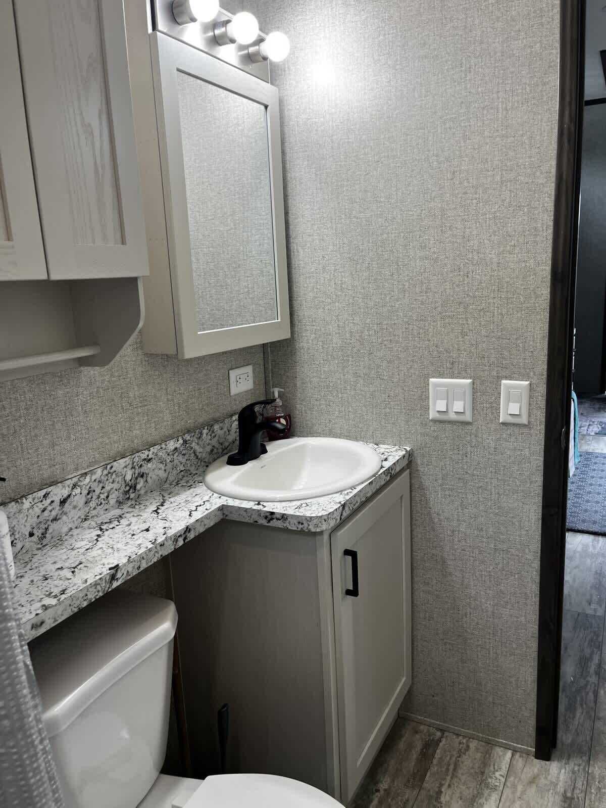 A bathroom with a white sink, a mirror with lights, a toilet, and a cabinet.