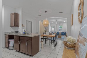 Eine moderne Küche mit Kochinsel, ein Essbereich mit Holztisch und Stühlen sowie ein Wohnzimmer mit blauen Sofas und einem großen Gemälde.