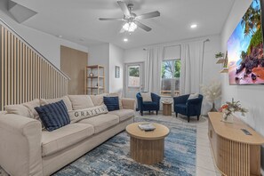 Ein modernes Wohnzimmer mit einer Couch, Sesseln, einem Couchtisch, einem Deckenventilator und einem großen Gemälde an der Wand.