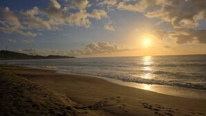Ein Strand mit Sonnenuntergang, Meereswellen und Fußspuren im Sand.