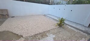 A patio area with a gravel floor, a wooden bench, and a potted plant. - Montes Vacation Home (Palo Seco)