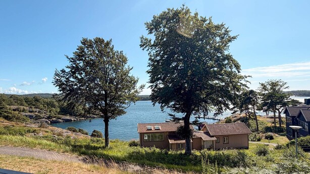 En fastighet vid sjön med en träaltan, ett litet hus och ett stort träd.