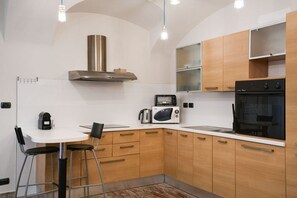A modern kitchen with a white countertop, wooden cabinets, a stainless steel range hood, a microwave, and an oven. - Torino | Il Vicolo Apartment (Torino)