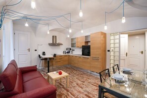 A compact living space with a kitchenette, a dining area with a glass table, and a red sofa. - Torino | Il Vicolo Apartment (Torino)