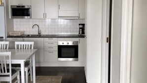 A modern kitchen with white cabinetry, a built-in oven, a coffee maker, and a dining area with white chairs. - 5 Star Holiday Home in Uddevalla (Uddevalla)