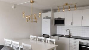 A modern kitchen with white cabinetry, a black countertop, and a chandelier with multiple light bulbs. - 5 Star Holiday Home in Uddevalla (Uddevalla)