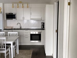 A modern kitchen with white cabinets, a stainless steel oven, a coffee maker, and a dining table with chairs. - 5 Star Holiday Home in Uddevalla (Uddevalla)