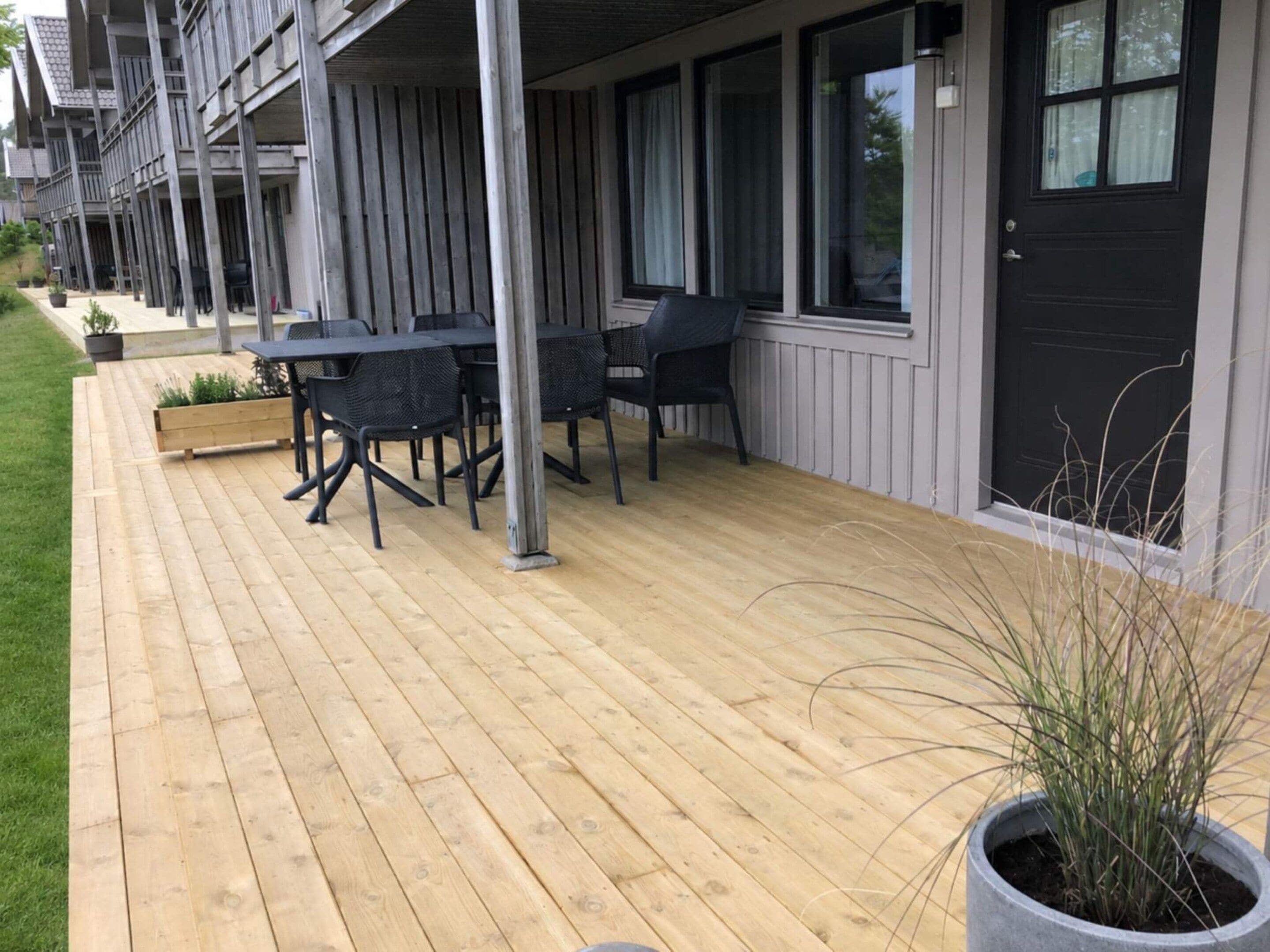 Une terrasse en bois avec des sièges d’extérieur et une plante en pot.