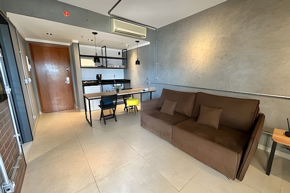 Una sala de estar moderna con un sofá, una mesa de comedor con sillas y una cocina con refrigerador y fregadero.