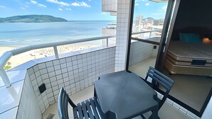 Un balcón con vistas a la playa y al océano, una mesa, sillas y un colchón.